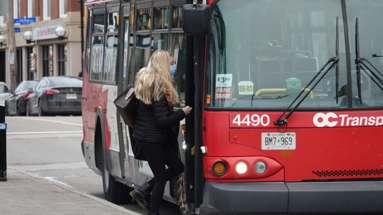 A person wearing a mask steps onto a red and white city bus.