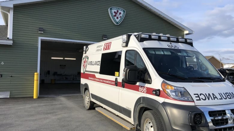 A white ambulance is parked at the bay of a green wooden building