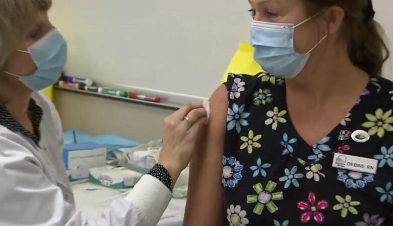 A nurse receives a COVID-19 vaccination from another nurse in a mask.