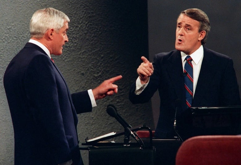 Two men in suits point fingers at each other from behind their respective podiums.