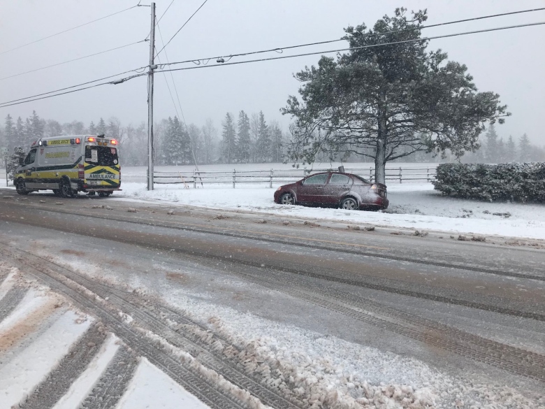 A car in the ditch beside a slushy road with an ambulance stopped nearby.