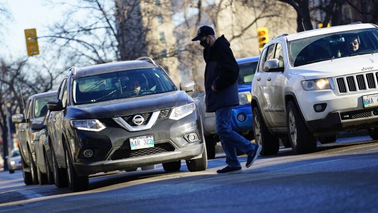 A man walks in front of a row of vehicles.