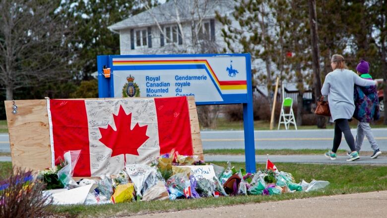 Photo of floral tributes and a signed Canadian flag in front of an RCMP sign.