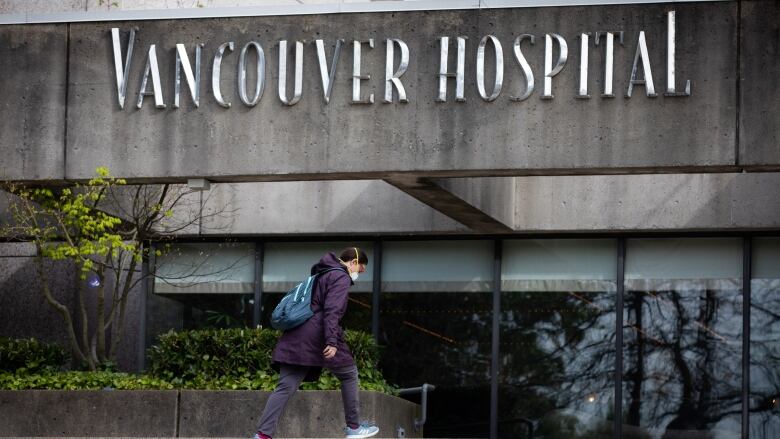 A woman wearing a facemask walks towards a building marked 'Vancouver Hospital'.