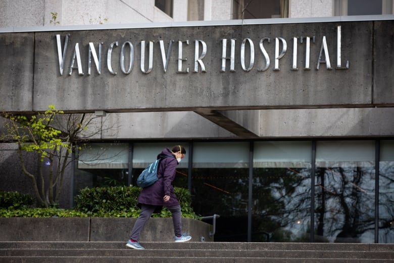 A woman wearing a facemask walks towards a building marked 'Vancouver Hospital'.