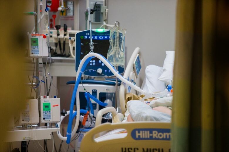 An unseen intubated person lies in bed in an ICU room.