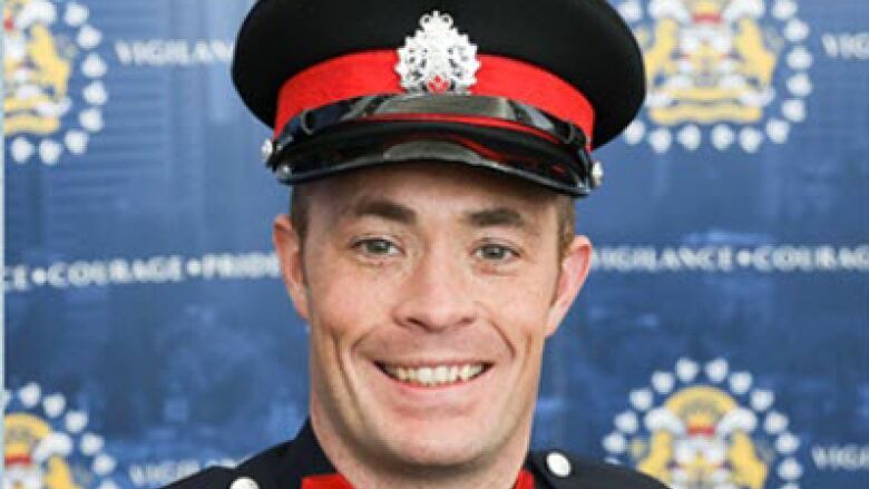 A Calgary police in his dress uniform poses in front of a wall of police logos.