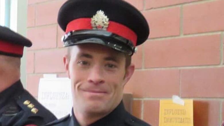 A police officer wearing his dress uniform stands in front of a brick wall.