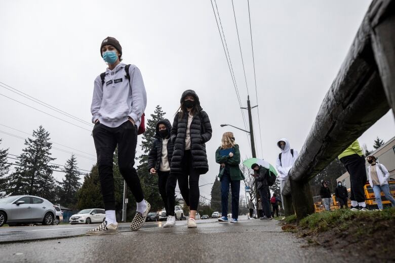 Students wearing masks walk in the rain outside Earl Marriott Secondary School. 