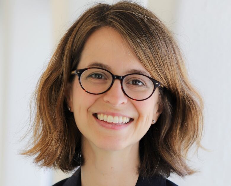 A woman in a black blazer and circular-framed glasses is pictured.