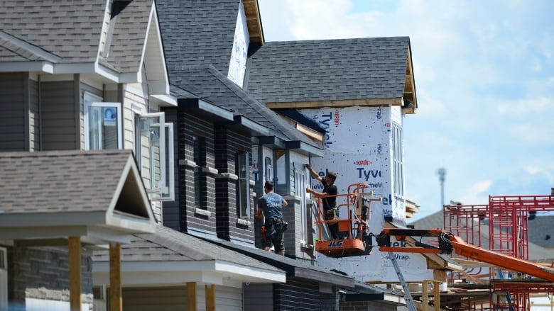 Construction workers put the finishing touches on houses being built in a new development of condos with peaked roofs.