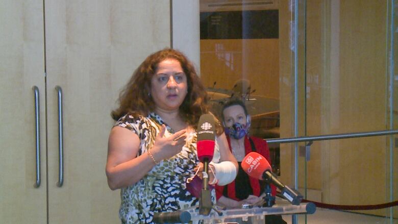 A woman stands before a podium gesturing with her hands. 