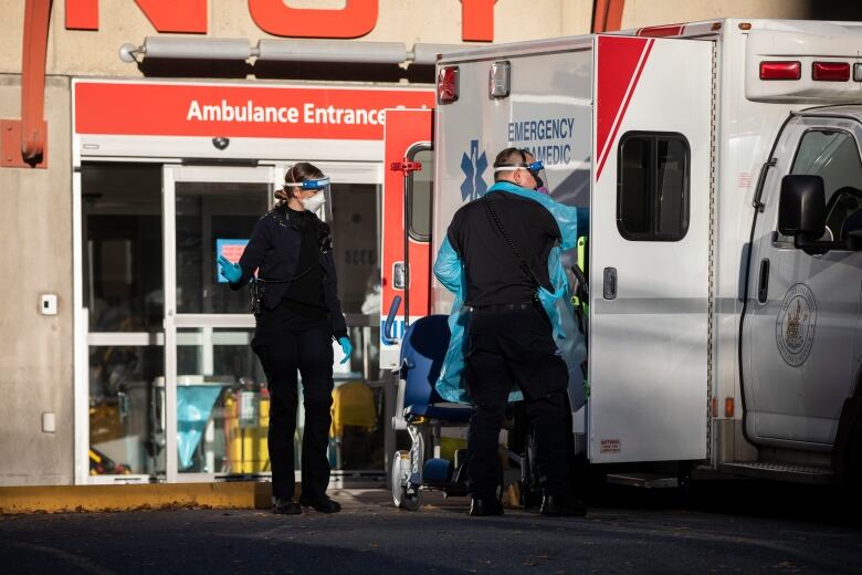 Two paramedics wearing facemasks remove something from an ambulance.