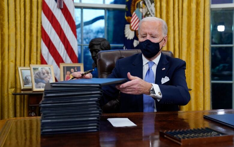 The President signs a stack of documents in black folders.