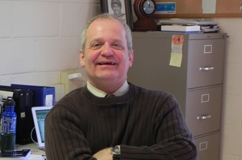 A man folding his arms and smiling while sitting at a desk