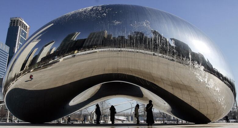 A metallic mirrored artwork with people underneath.