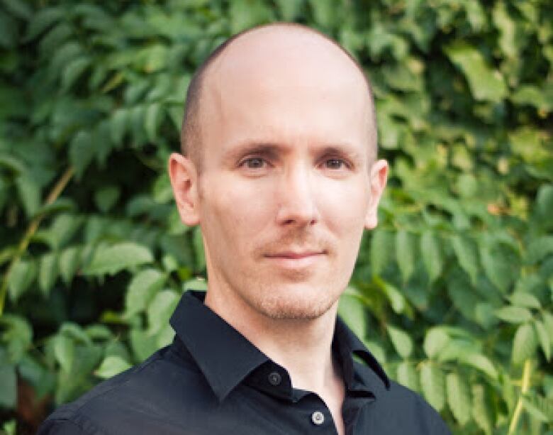 A man wearing a black dress shirt looks into the camera