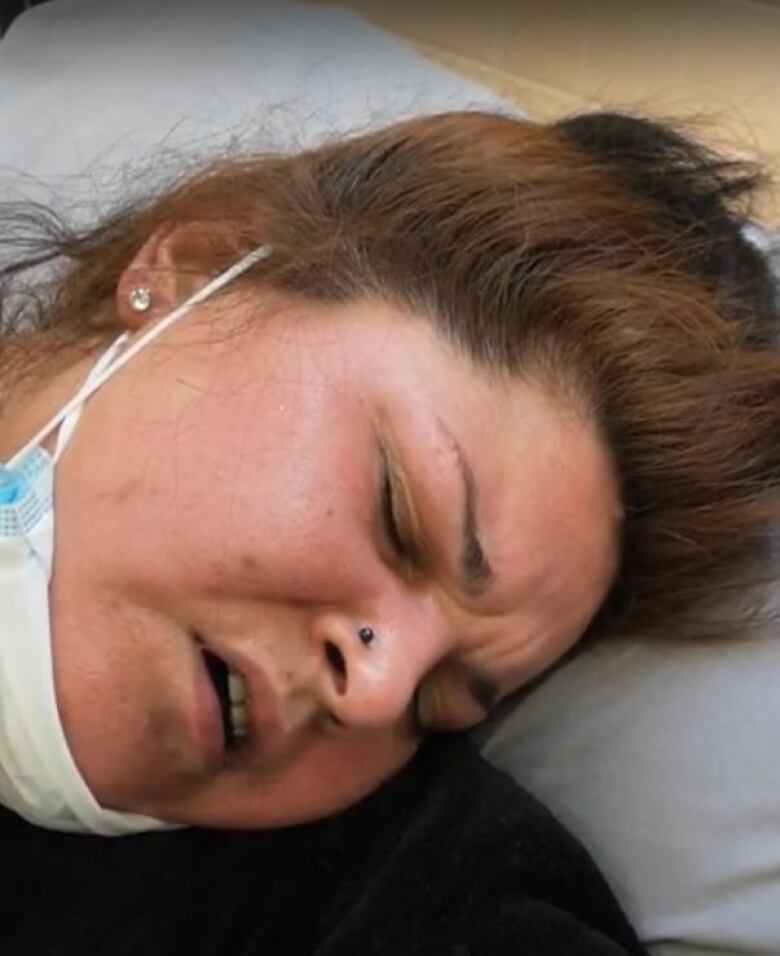 A woman's face as she appears to lie on her side. She appears to be in pain.