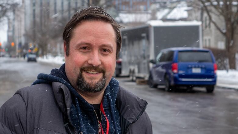 A man poses for a photo outside in a city on a snowy day.