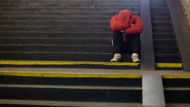 A man wearing a red jacket holds his head in his hands while sitting on stairs.