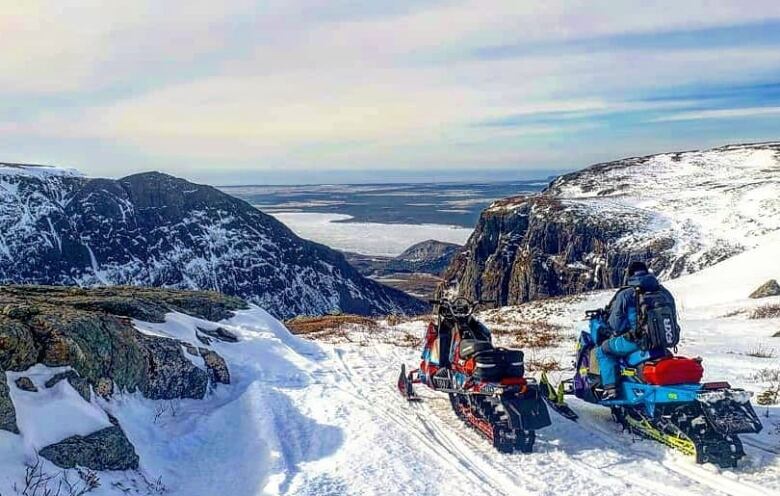 Two snowmobiles parked on top of a cliff. 