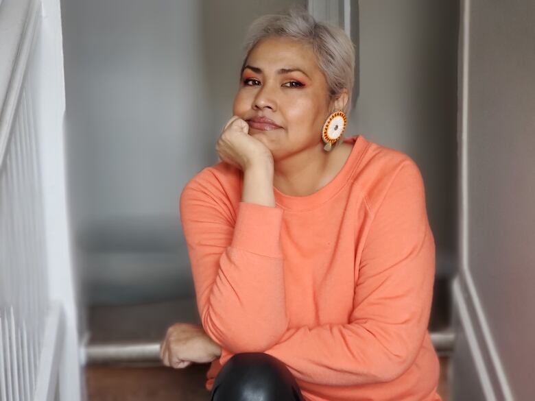 A woman in an orange shirt poses for a photo.