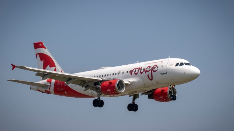 An Air Canada Rouge plane flies through the sky.