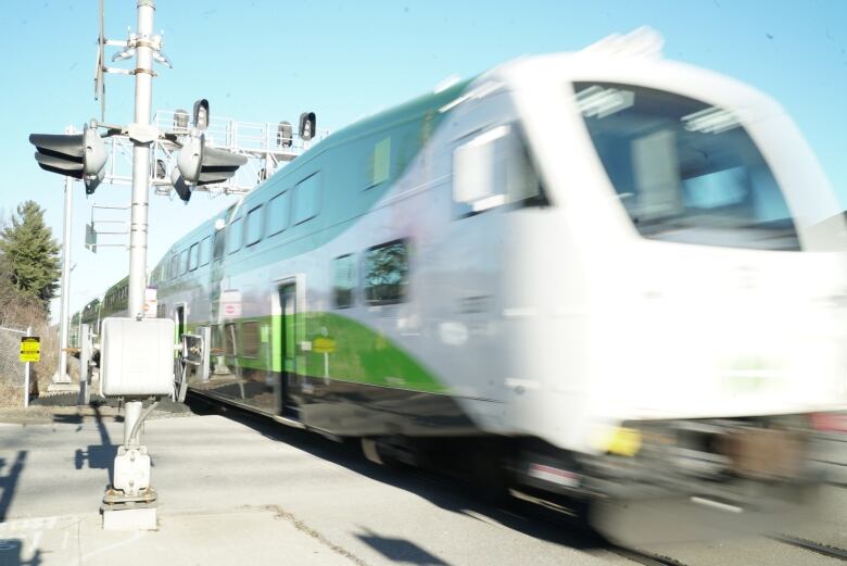 A GO Train speeds into a station on a sunny day. It is viewed from the edge of the platform.