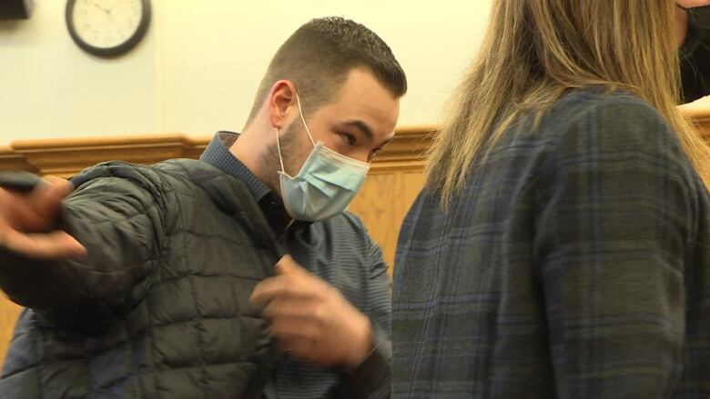 A younger man with cropped brown hair puts his arm in a black puffer jacket. 