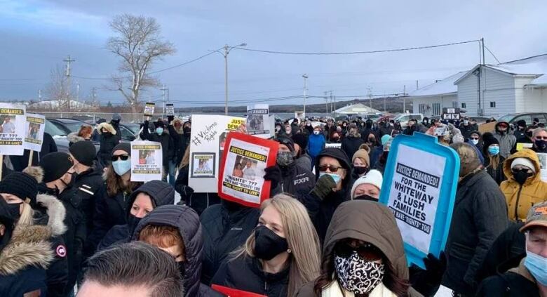 Dozens of people wearing thick winter clothing hold signs demanding justice. 