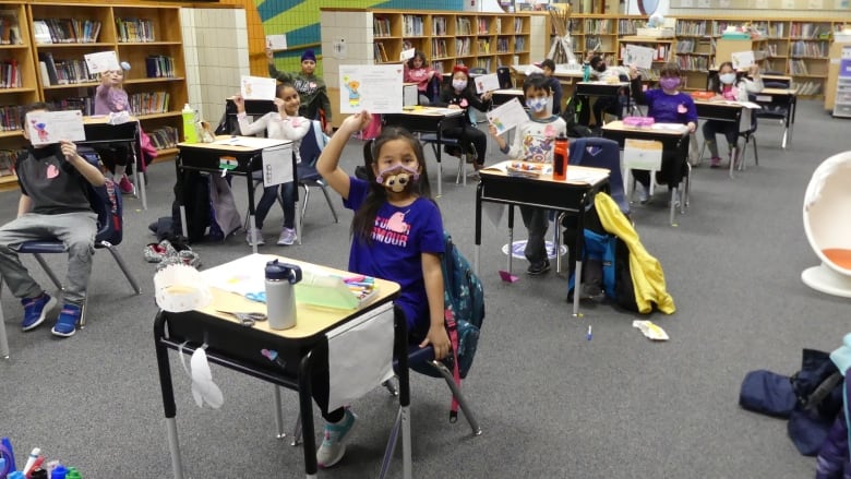 Young kids in a classroom hold up signs. 