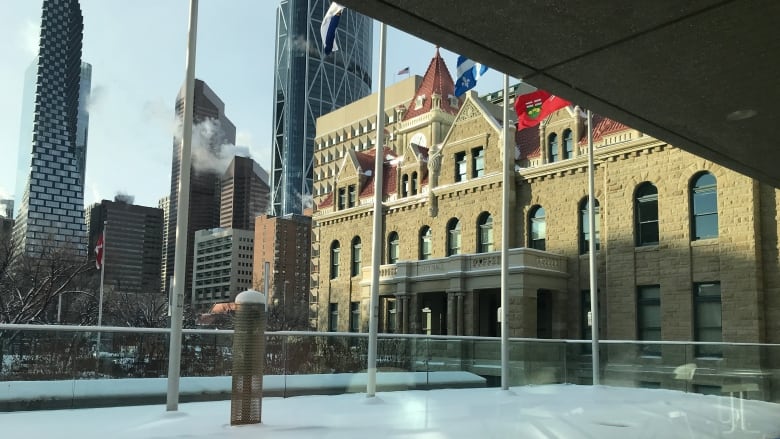 a building stands in front of larger, newer buildings. there is snow on the ground in front.