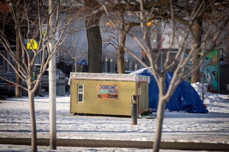 A picture of a small wooden shelter in a Toronto park that has a sign saying someone lives here.