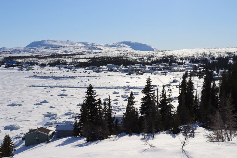 A snow covered landscape shows mountains, trees and houses along with two wharfs. 