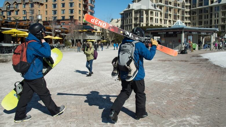 A skier and snowboarder walk with their gear in Whistler, B.C.