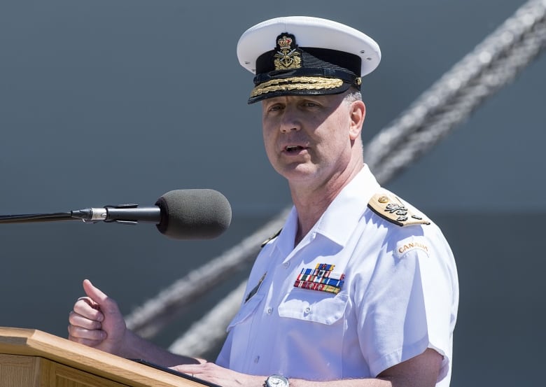 A man wearing a navy uniform speaks at a podium.