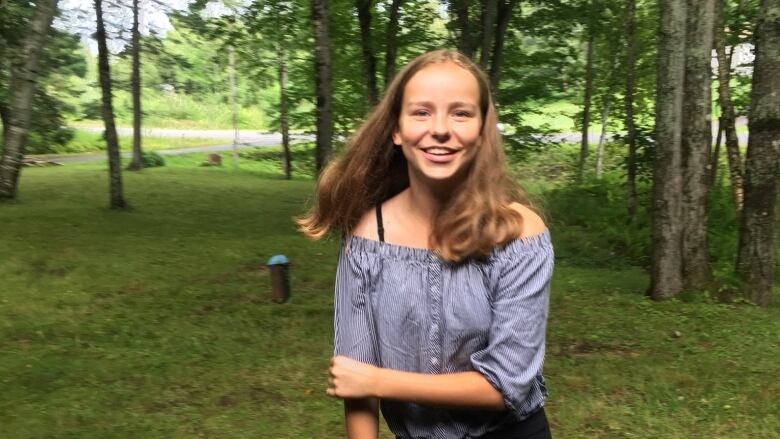 A portrait of a smiling teenage girl in a grassy area, surrounded by trees.