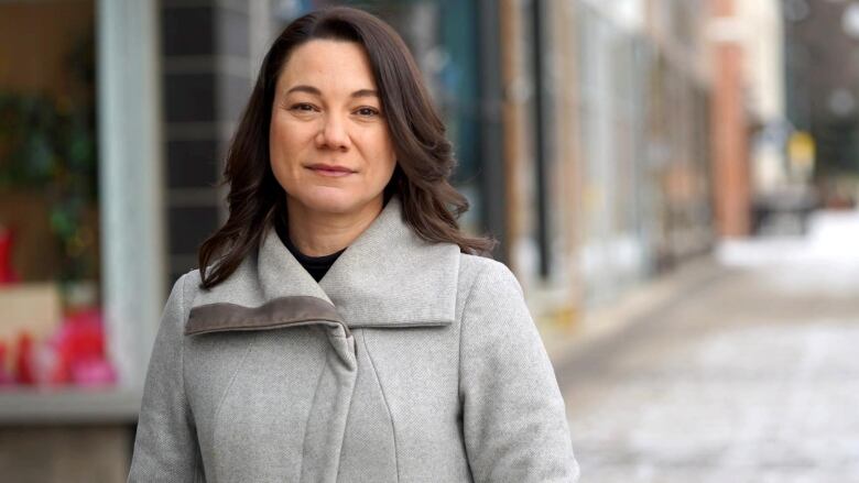  a woman stands in a jacket on a city street.