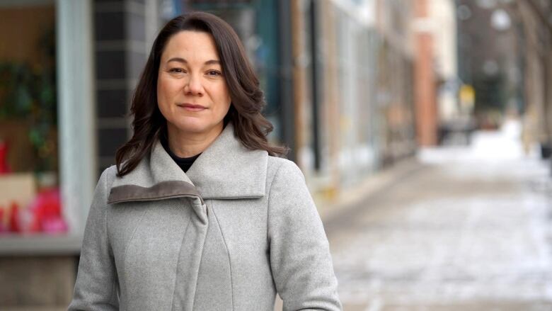  a woman stands in a jacket on a city street.