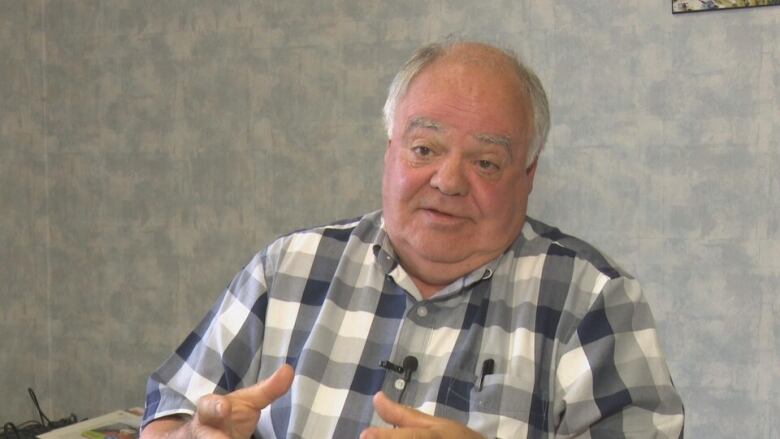 A bald man with a white fringe and a checkered shirt is speaking.