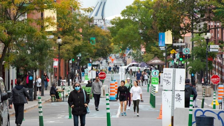 People wearing masks walk down a street in Montreal. Cars have been barred from the area with blockers.