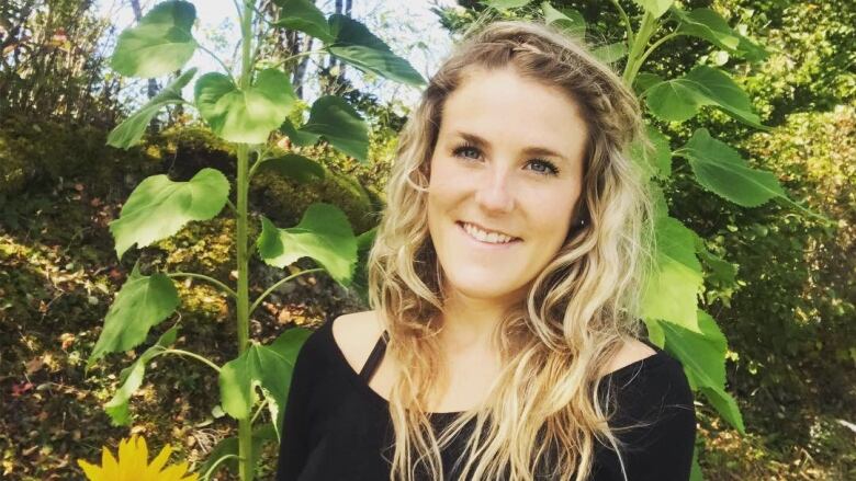 A smiling young woman surrounded by several sunflowers. 