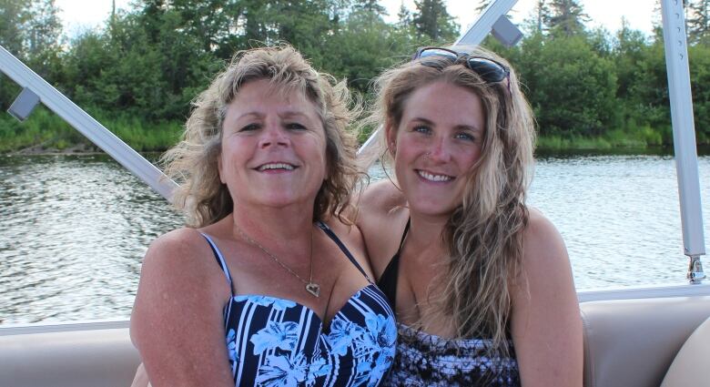 A mother and daughter, arm in arm, on a boat with water in the background. 