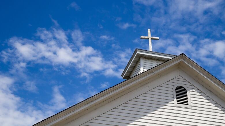 A wooden cross on a simple steeple set against a sunny summer blue sky.