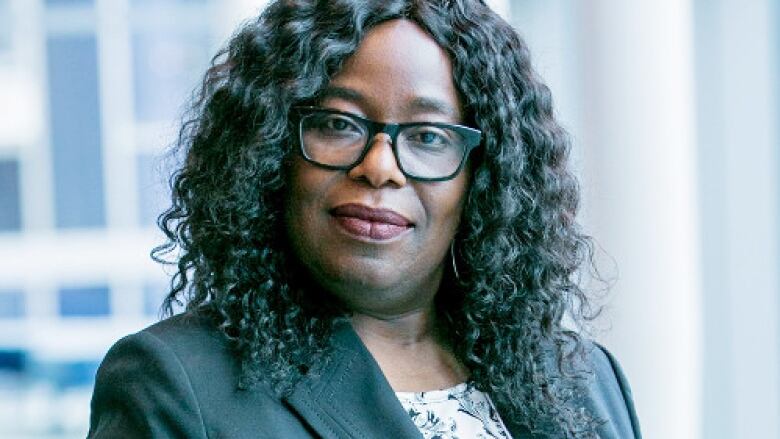 A Black woman with dark curly hair wearing glasses and a black blazer