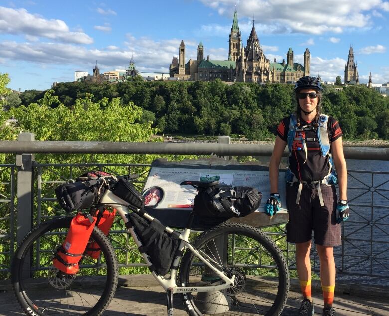 A woman poses in front of Parliament from the Quebec side with her bike on a sunny day