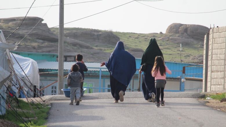 Women and children walk down a road in a detension camp in Syria.