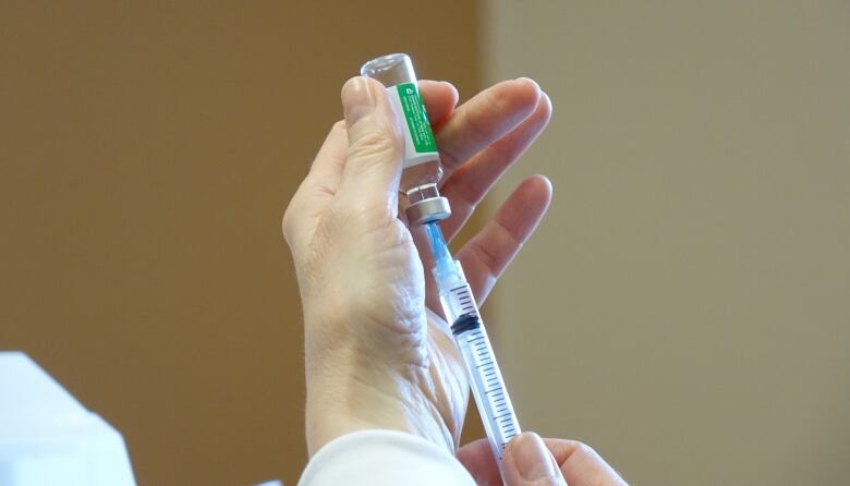 A closeup of hands inserting a syringe into a glass vaccine vial.