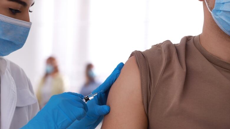 A medical worker gives a vaccine dose to a person in a clinic, with other patients in the background.