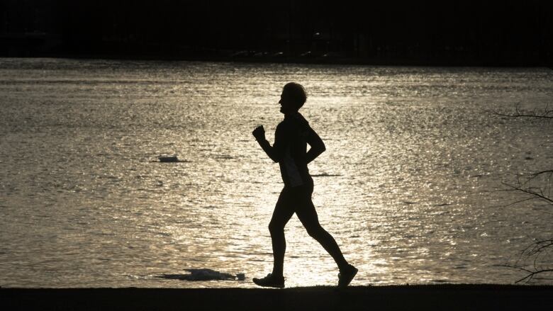 A runner's silhouette next to a river than has a few chunks of snow in it.